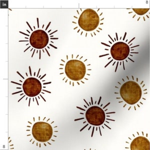May include: A white background with a repeating pattern of brown and gold suns. The suns have a textured look and are outlined in brown.