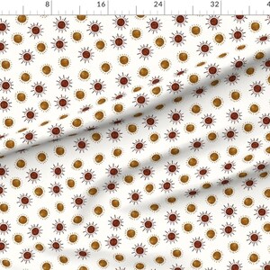 May include: White fabric with a repeating pattern of brown and gold suns. The suns have a simple, hand-drawn style with radiating lines.