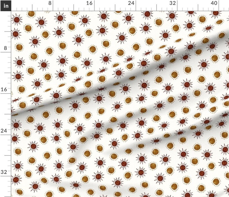 May include: White fabric with a repeating pattern of brown and gold suns. The suns have a simple, hand-drawn style with radiating lines.
