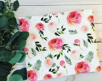 May include: White fabric with a pink and green watercolor floral pattern. The fabric features a repeating pattern of pink roses, green leaves, and small pink buds.
