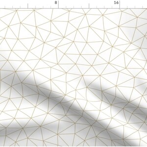 Op de afbeelding: Witte stof met een geometrisch patroon van dunne gouden lijnen die driehoeken vormen.