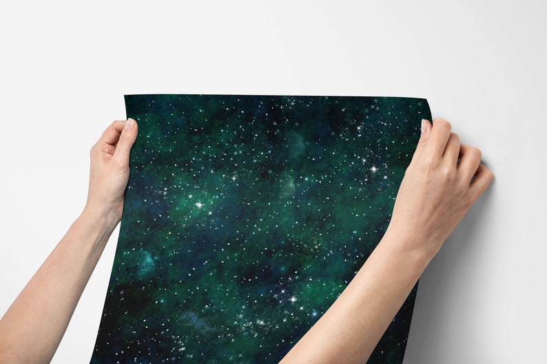 K&ouml;nnte beinhalten: Die H&auml;nde einer Person halten ein Blatt dunkelgr&uuml;nes und blaues Tapetenpapier mit einem Galaxie-Druck. Die Tapete ist mit wei&szlig;en Sternen bedeckt.