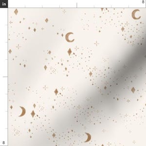May include: Off-white fabric with a celestial pattern featuring gold crescent moons, diamond shapes, starbursts, and tiny dots. The design is evenly distributed across the fabric, creating a dreamy, whimsical aesthetic. The fabric is 8 inches wide.