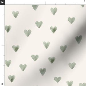 May include: Cream-colored fabric with a repeating pattern of watercolor-style sage green hearts. The hearts are evenly spaced and vary slightly in shade, creating a soft, textured appearance. The fabric is likely suitable for various craft and home decor projects.