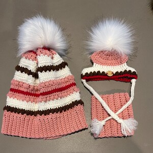 Puede incluir: Dos gorros de punto con pompones blancos. El gorro m&aacute;s grande es rosa, blanco, marr&oacute;n y rojo con un patr&oacute;n a rayas. El gorro m&aacute;s peque&ntilde;o es rosa, blanco, marr&oacute;n y rojo con un patr&oacute;n a rayas y un cuello de punto rosa a juego.
