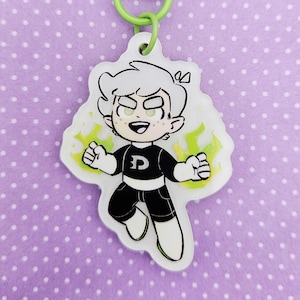 May include: A cartoon keychain featuring a character with white hair, wearing a black and white outfit with a "D" on the chest. The keychain has a green clasp and a green ring. The character is surrounded by green energy.
