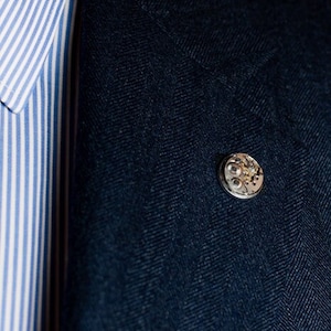 Pu&ograve; includere: Un blazer blu scuro con una spilla argentata con un design circolare con dettagli intricati.