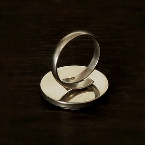 May include: A silver ring with a round, flat base. The ring is made of metal and has a smooth, polished finish.