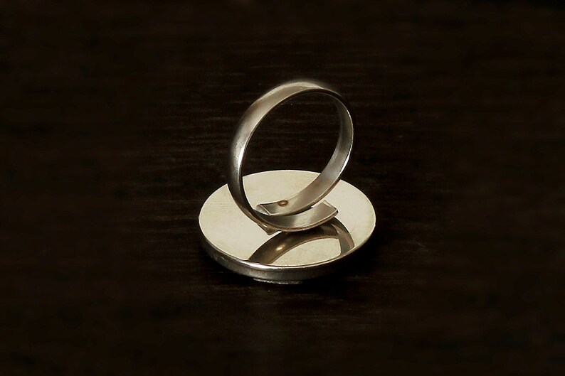 May include: A silver ring with a round, flat base. The ring is made of metal and has a smooth, polished finish.