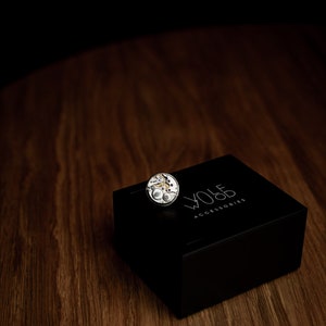 Pu&ograve; includere: Un movimento di orologio argentato su una scatola nera con il testo "WOLF ACCESSORIES" stampato sulla parte superiore.