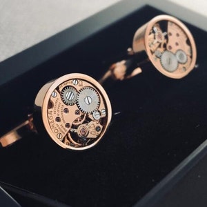 May include: A pair of rose gold cufflinks with a visible watch mechanism. The cufflinks feature the text "OMEGA" and "17 JEWELS" on the face.
