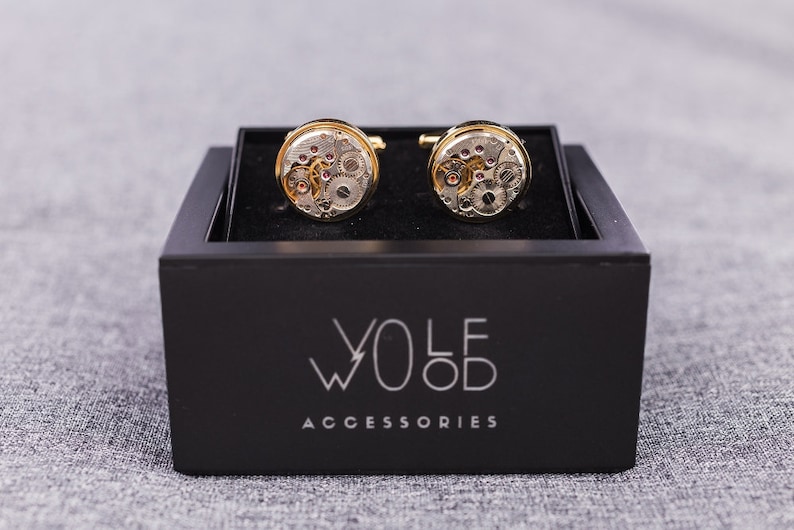 May include: A pair of gold cufflinks with a watch movement design, displayed in a black box with the text "WOLF ACCESSORIES".