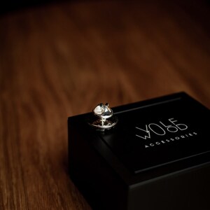 May include: A silver tie tack in a black box with the text "WOLF ACCESSORIES" on the lid.
