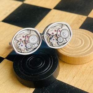 May include: A pair of silver cufflinks with exposed watch mechanisms. The cufflinks feature the text "OMEGA SWISS 17 JEWELS".