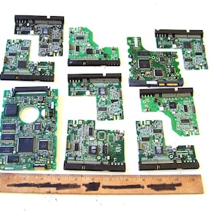 May include: A collection of eight green printed circuit boards of varying shapes and sizes, featuring black connectors and integrated circuits, arranged above a wooden ruler measuring 30 cm in length.