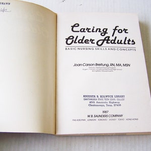 May include: Open book titled "Caring for Older Adults" with text about basic nursing skills and concepts. The author is Joan Carson Breitung. Published by W.B. Saunders Company in 1987. The book is from the Augusta R. Kolwyck Library.