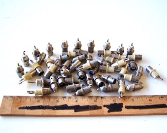 Könnte beinhalten: Eine Sammlung von Vintage-Zündkerzen, bestehend aus Metall und Keramik. Die Zündkerzen sind auf einer weißen Oberfläche verstreut, mit einem Holzlineal zur Größenbestimmung. Die Zündkerzen scheinen gebraucht zu sein.