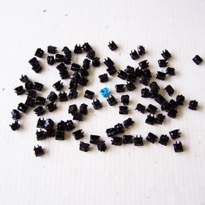 Puede incluir: Una colección de teclas de teclado mecánico negras con una tecla azul en el centro.