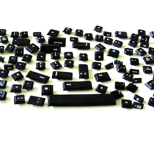 May include: A collection of black keyboard keys scattered on a white surface. The keys are of various sizes and shapes, including the space bar, Enter, Shift, and other letter and number keys. Some keys have white lettering.