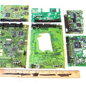 May include: Five green printed circuit boards of varying rectangular shapes and sizes, featuring integrated circuits, capacitors, and black connectors, arranged above a wooden ruler measuring up to 12 inches in length.