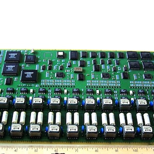 May include: A green circuit board with numerous electronic components, including chips, capacitors, and connectors. The board has a rectangular shape and is approximately 12 inches long. It is designed for electronic devices.