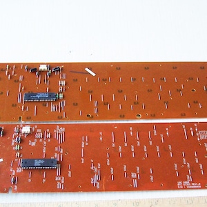 May include: Two brown circuit boards with electronic components, including chips and resistors. The boards are arranged vertically, with the top board slightly offset to the right. The boards are labeled with numbers and letters.