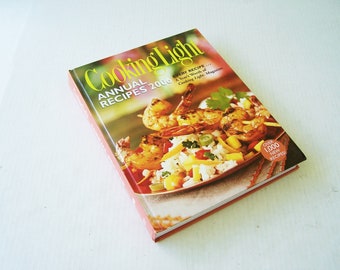 Puede incluir: Un libro de cocina titulado "Cooking Light Annual Recipes 2000" con una foto de un plato de camarones y arroz en la portada. El texto "Over 1,000 New Recipes" está en un círculo rojo en la portada.
