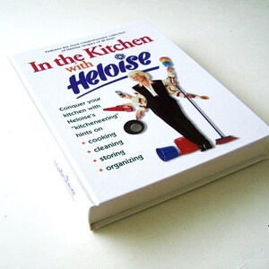 May include: A white book titled "In the Kitchen with Heloise" features a woman holding various kitchen tools and cleaning supplies. The book cover includes the text "Conquer your kitchen with Heloise's "kitcheneering" hints on cooking, cleaning, storing, and organising."