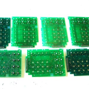 May include: Seven rectangular green printed circuit boards arranged in two rows. Each board features a grid of circular contact points, metallic traces, and a multi-pin connector along one edge. The boards vary slightly in shade and component layout.