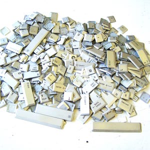 May include: A large pile of loose, light gray computer keyboard keys scattered together. The collection includes various alphanumeric keys, function keys, and long space bars, all featuring black printed letters, numbers, and symbols.