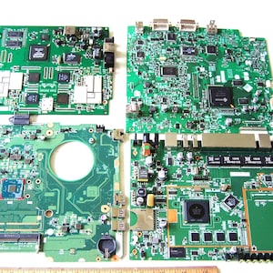 Pode incluir: Quatro placas de circuito impresso verdes dispostas numa grelha. Cada placa apresenta vários circuitos integrados, condensadores e conectores. Uma régua de madeira é visível na parte inferior, mostrando medidas em centímetros.