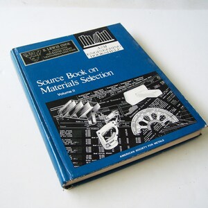 May include: A blue hardcover book titled "Source Book on Materials Selection, Volume II" by E. Lewis Cook and Associates. The book cover features a black and white illustration of various engineering tools and diagrams. The book is published by the American Society for Metals.