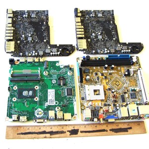 May include: Two black rectangular circuit boards, one green HP motherboard, and one tan motherboard with various electronic components, ports, and slots. A wooden ruler is placed at the bottom, showing a length of approximately 30 cm.