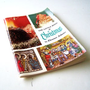 May include: A vintage paperback book titled "The Little Book of Christmas" by Eleanor Adams. The cover features illustrations of a Christmas pudding, a nativity scene, and a family gathered around a fireplace.