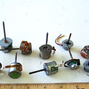 May include: A collection of ten small, silver-coloured electric motors with metal shafts. The motors have various labels and markings, including "SONY" and "MOTOR".