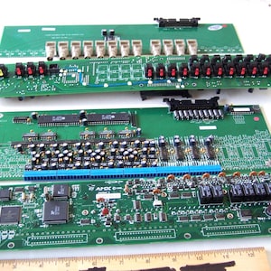 May include: Three green circuit boards with various electronic components, including resistors, capacitors, and connectors. The boards are arranged in a stack, with the top board having a row of red and black switches.