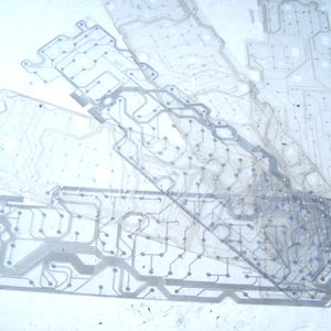May include: A collection of translucent, flexible keyboard membrane sheets featuring intricate, dark gray printed circuitry patterns, conductive traces, and circular contact points layered over one another in a stacked arrangement.