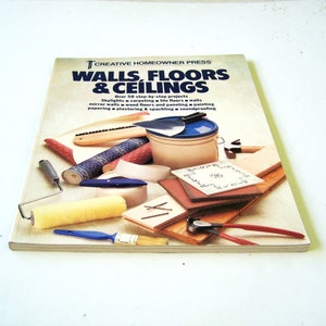 Puede incluir: Un libro titulado "WALLS, FLOORS & CEILINGS" con diversas herramientas y materiales de bricolaje. La portada presenta texto e imágenes de proyectos como tragaluces, pintura y pisos. Las herramientas incluyen un rodillo de pintura, un pincel y una espátula.