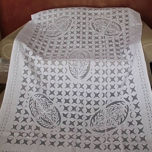 May include: White lace tablecloth with a repeating pattern of four-pointed stars and oval designs. The oval designs feature a stylized floral motif.