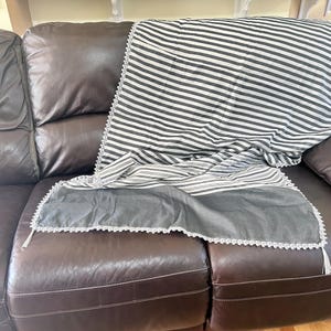 May include: A brown leather sectional sofa with a white and black striped throw blanket with a white crocheted trim.