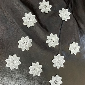 May include: Ten white lace flower appliques on a black leather surface.