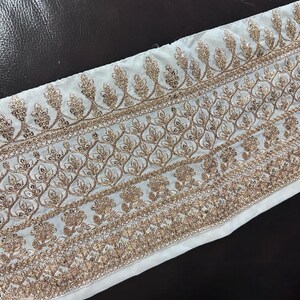May include: White fabric trim with gold embroidery featuring a repeating leaf pattern. The trim has a scalloped edge.