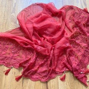 May include: A red sheer scarf with embroidered floral details and beaded trim. The scarf has a scalloped edge and features tassels on each corner.