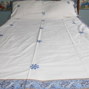 May include: White bedspread with a blue paisley border and blue embroidered flowers.