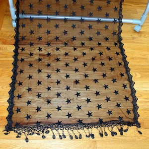 May include: Black sheer fabric with a star pattern and a lace trim. The fabric has a fringe along the bottom edge.