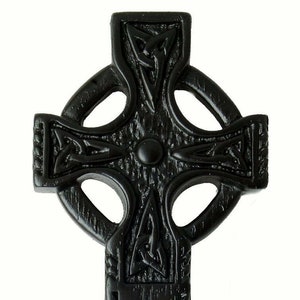 May include: Black wooden Celtic cross with intricate knotwork designs. The cross has a small bowl at the bottom.