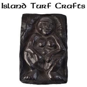 May include: A dark brown wooden sculpture of a seated female figure with a carved face and detailed features. The sculpture is set into a rectangular frame.