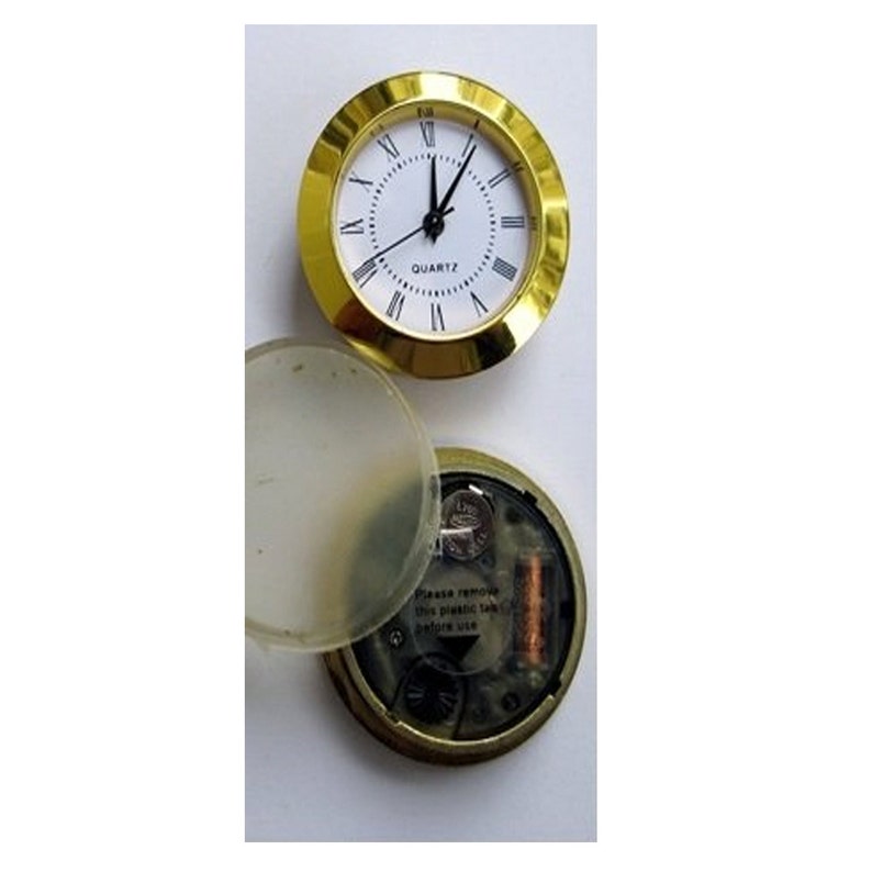 May include: A gold-colored clock with a white face and black hands. The clock is in a clear plastic case with a battery compartment on the back. The clock face reads "QUARTZ".