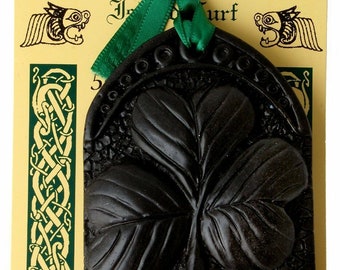 May include: Black shamrock-shaped decoration with the word "IRELAND" at the bottom. The decoration is attached to a yellow card with green accents and text. A green ribbon is used for hanging. The words "Island Turf Crafts" are at the top.