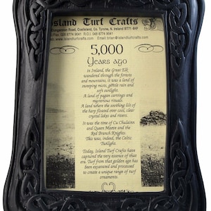 May include: A black framed picture with a beige background and text that reads "Island Turf Crafts" and "5,000 Years ago". The text describes the history of turf in Ireland and how it is used to create ornaments.